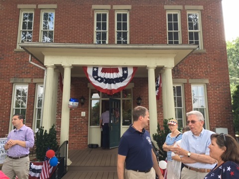 Visitors standing near entrance to brick museum building with red white and blue bunting hanging from front porch