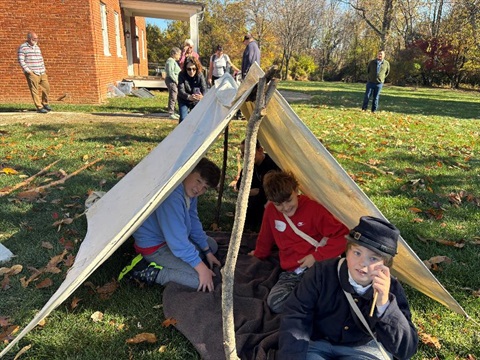 Kids sitting in Civil War Era tent with historic house behind them