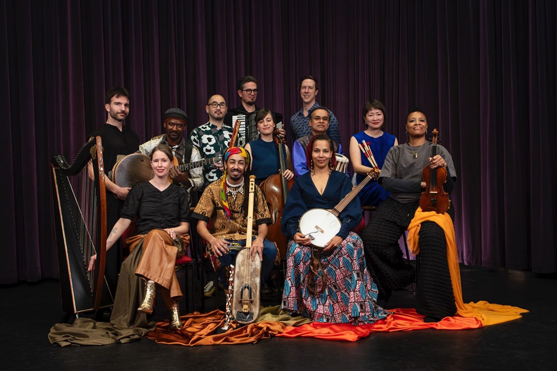 Group of men and women seated and standing in colorful dress holding a variety of instruments facing the viewer 